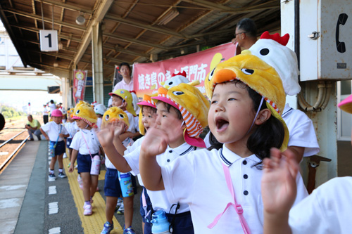 ニワトリとヒヨコの帽子をかぶった深川幼稚園の園児が列車に手を振る