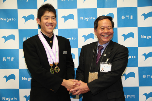 2つのメダルを首にかけ、市長と握手する村岡翼輝さん（左）